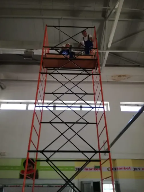 Работники на строительной лесах высотой 2 метра внутри помещения, с платформой для работы