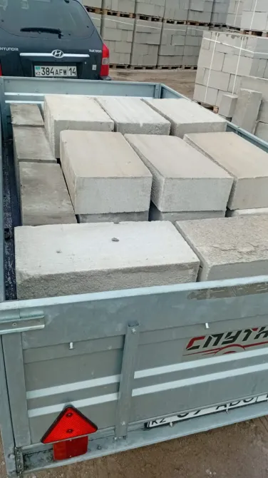 Парковка алаңының фонында орналастырылған бетон блоктары, автомобильдің тіркемесінде.