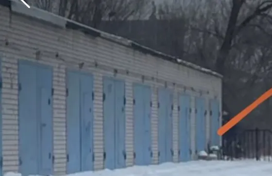 снег на земле перед складскими помещениями с голубыми дверьми и деревьями на фоне