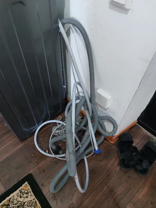 Кір жуу машинасының жанындағы еденде үгіту шлангтары