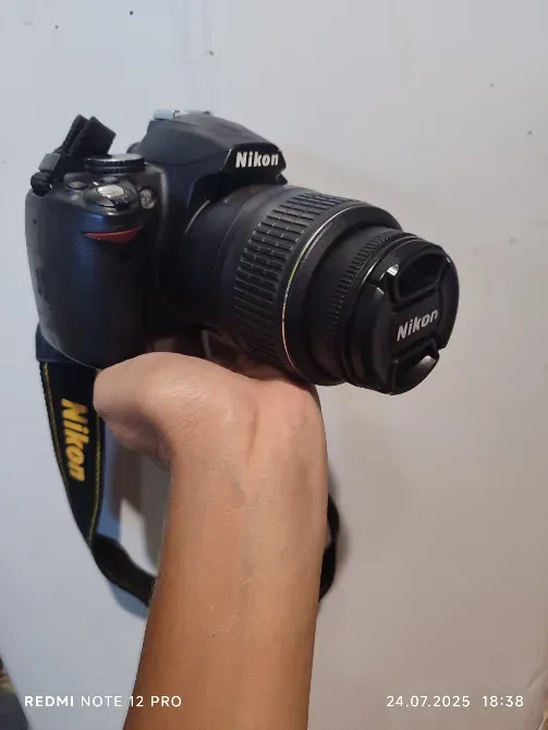 камера Nikon с объективом и ремешком в руках