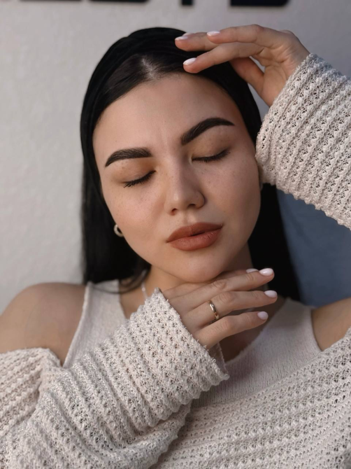 Молодая женщина с закрытыми глазами позирует, прикрыв лицо руками