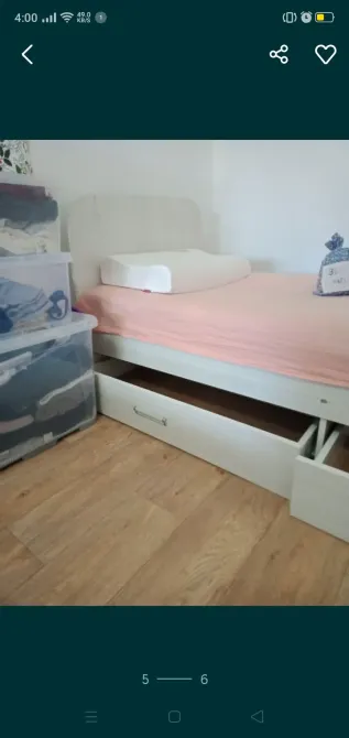 Кровать с розовым матрасом и подъемными ящиками, рядом пластиковые контейнеры с вещами