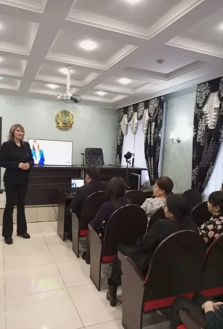 Тыңдармандары көп залда материал ұсынып жатқан әйел