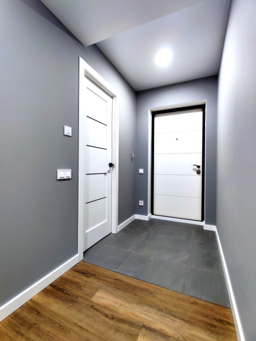 Современный коридор с серыми стенами и светлыми дверями, пол с плиткой и деревянными элементами
