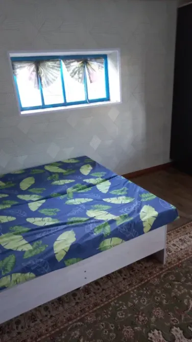 Спальня с кроватью и большим окном, на покрывале изображены листья