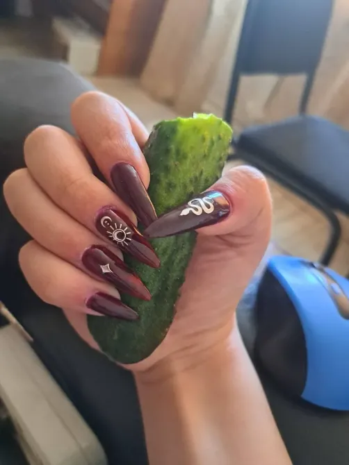 Длинные ногти с фиолетовым лаком, держащие огурец