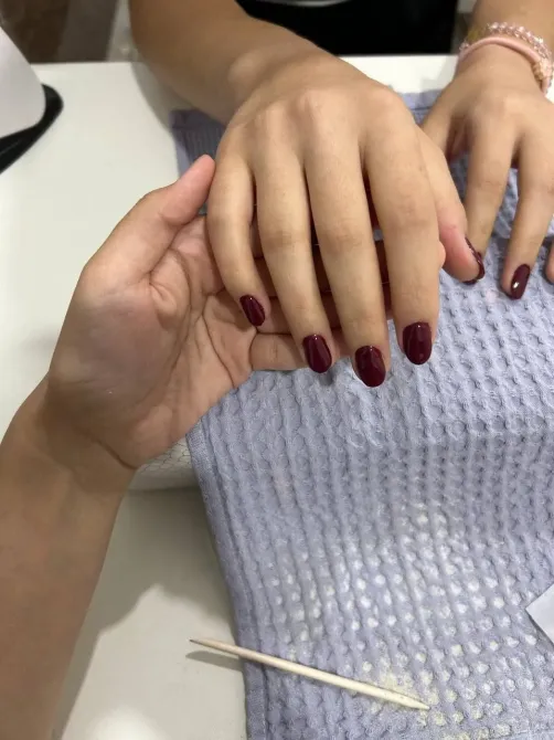 Руки с короткими бордовыми ногтями на фоне текстуры