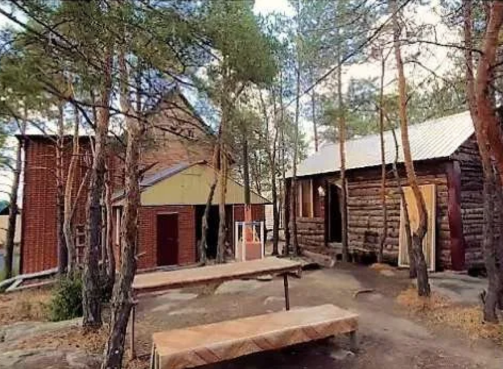 Два строения на даче, одно из которых бревенчатое, окружают камни