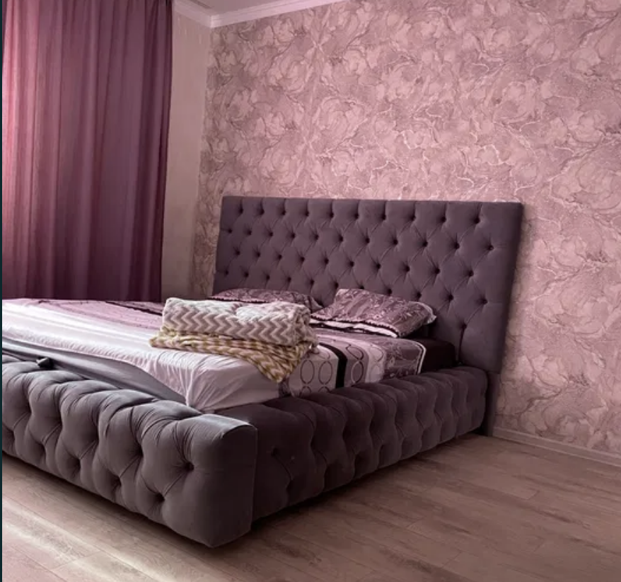 Комфортабельная двуспальная кровать с мягким изголовьем на фоне розовых штор