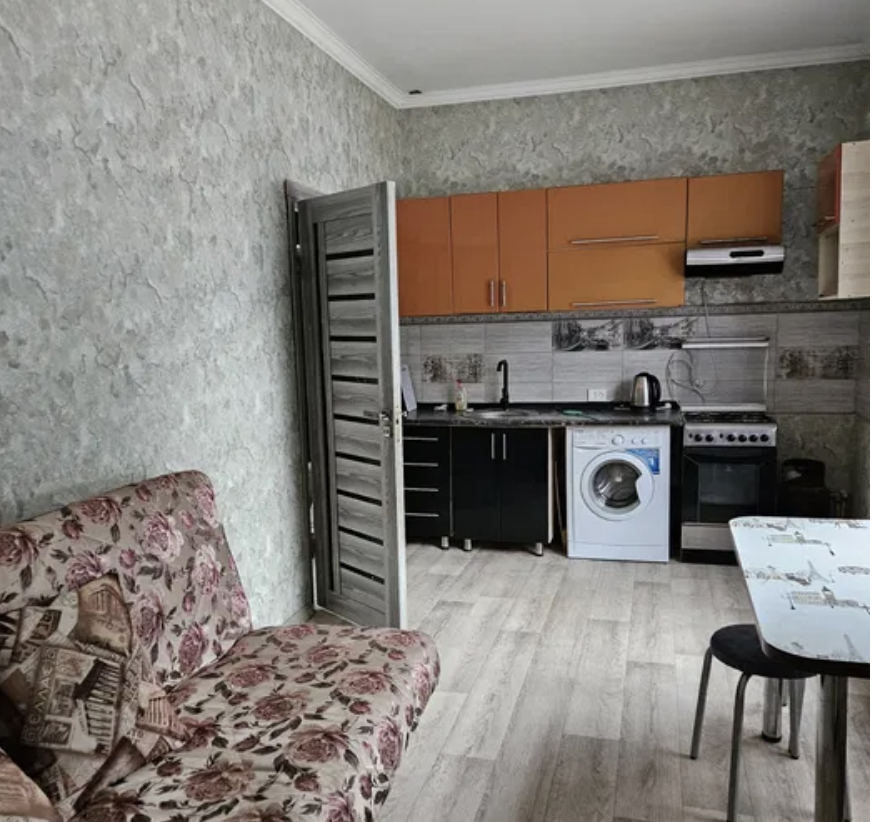 Кухня с зеленовато-серой стеной, диваном с цветочным рисунком, стиральной машиной и плитой