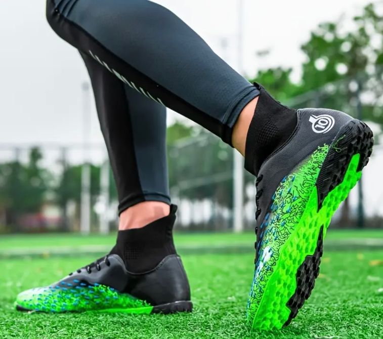 Ойыншының аяғында, жасыл алаңда анық көрінетін жарқын дизайн элементтерімен кроссовкалар