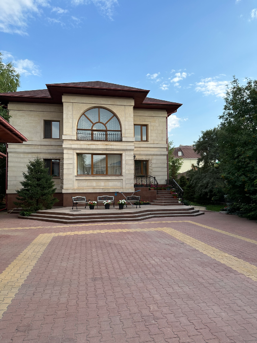 Вид на дом с большим окном и террасой, окружающей зеленую зону с цветами и деревьями