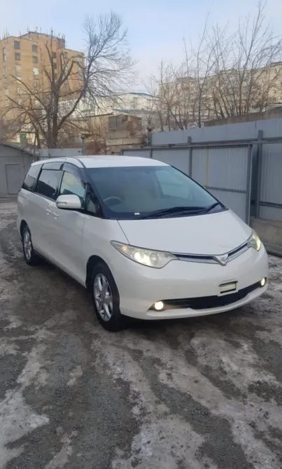 Белый минивэн Toyota с включенными фарами на фоне зимнего пейзажа