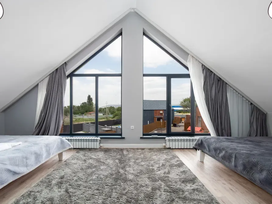 Интерьер комнаты с треугольной крышей и большими окнами, оформленной в светлых тонах