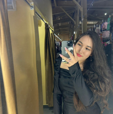 Ұзын шашты қыз қара көйлекте дүкенде айна алдында тұрған позада.