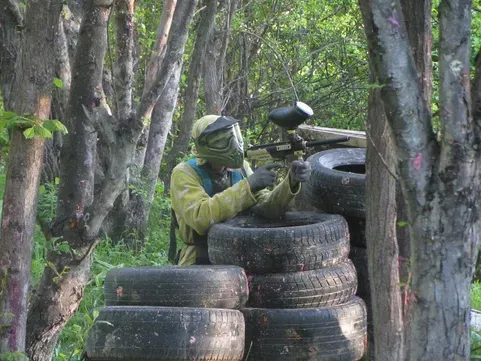 Игрок в страйкбол, прячущийся за покрышками в лесу