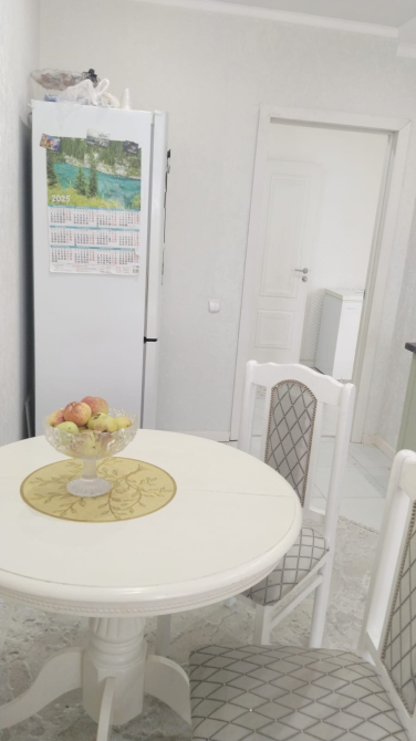 Кухня с холодильником и украшенным фруктами столом, светлые стены и спокойная обстановка