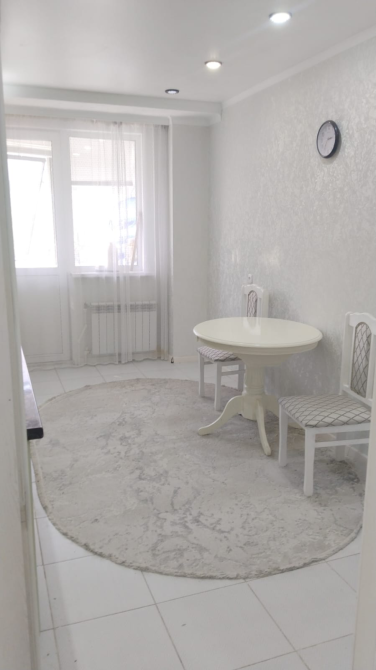 Уютная кухня с круглым столом и стульями, светлые стены и круглой коврикой