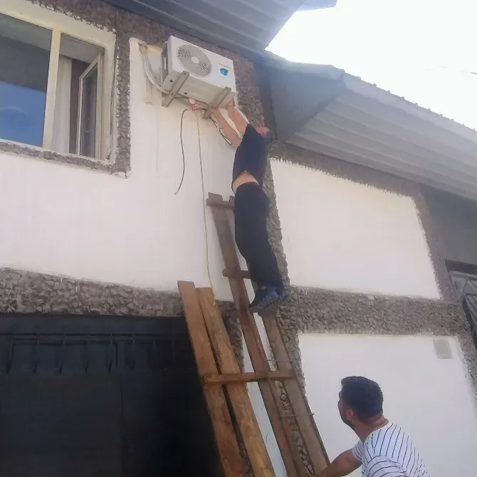 Два человека на лестнице, устанавливающие кондиционер на стене здания