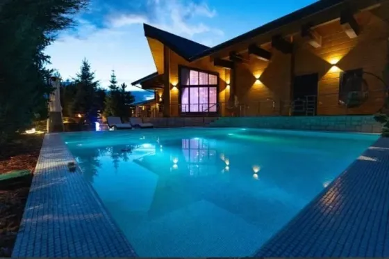 Бассейн на открытом воздухе с вечерним освещением и деревянным домом на фоне