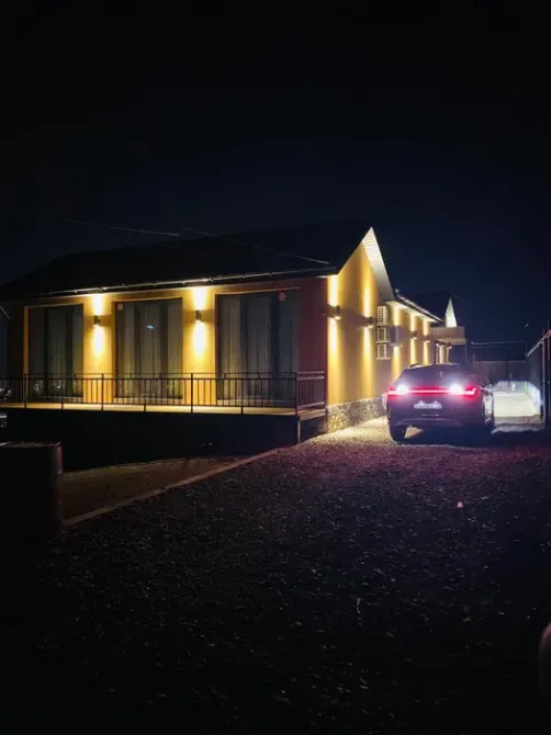Деревянный дом с подсветкой и автомобилем на парковке ночью