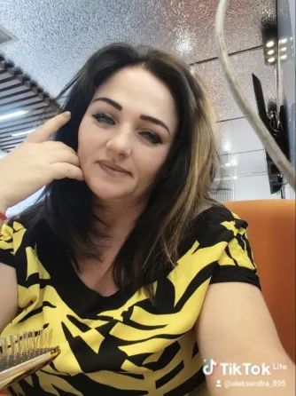 Женщина с длинными тёмными волосами и платьем с жёлто-чёрным узором, улыбается в кафе