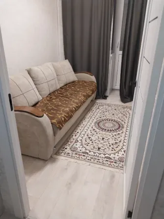 Уютты бөлме, бежевый диван және жеңіл едендегі кілем, сұр перделер.