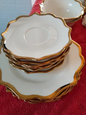 Ақ тарелкалар, алтын жиектерімен, қызыл матаның үстінде әдемі орналастырылған