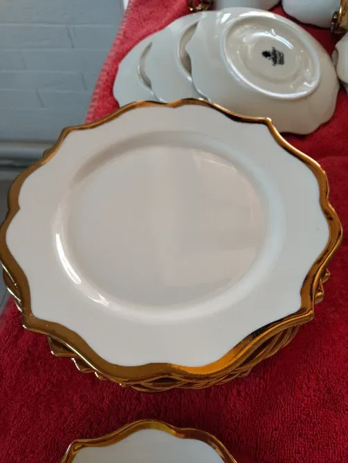 Ақ тарелкалар, алтын жиектерімен, қызыл матаның үстінде әдемі орналастырылған