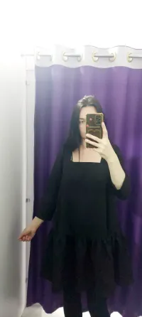 Қара көйлек киген қыз фиолет түсті перделермен безендірілген айна алдында тұр.