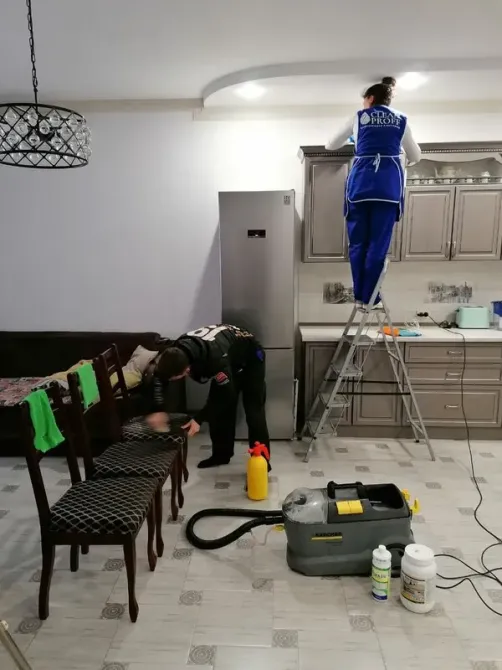 Специалист по уборке выполняет работу на кухне, используя чистящие средства и оборудование