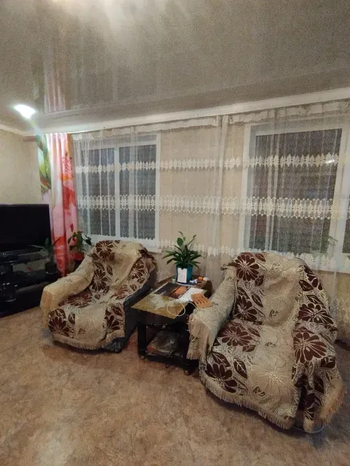 Екі кресло мен үстел бар бөлме, үстел үстінде заттар қойылған