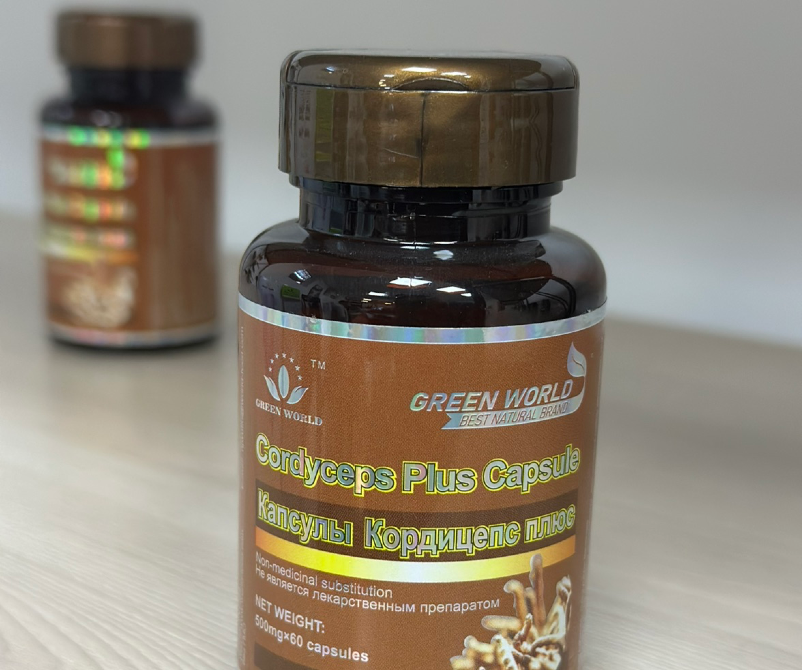 Green World-тың Cordyceps Plus капсулаларының бөтелкесі басқа қаптаманың бұлыңғыр суретінің фонында