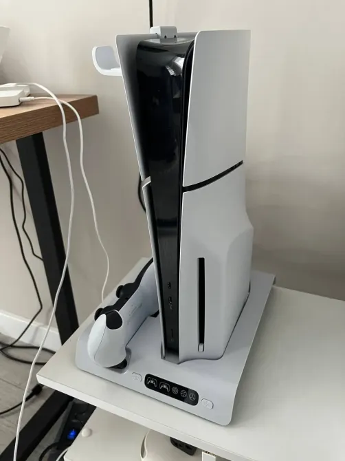 Игровая консоль PlayStation 5 с видимой боковой стороной и контроллером на подставке