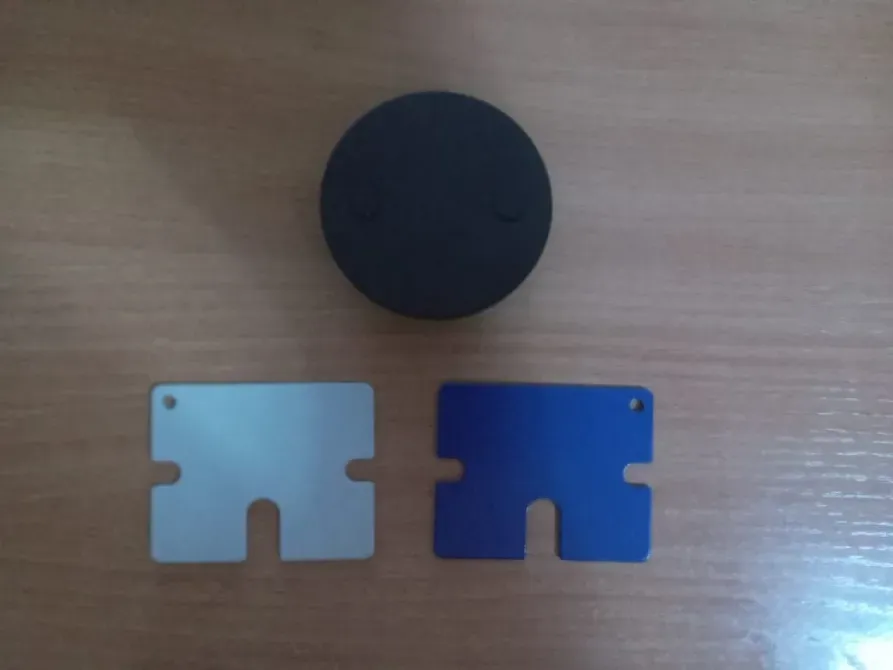 Стол үстінде үш зат: қара дөңгелек нысан және көк пен күміс түсті екі пластикалық карта