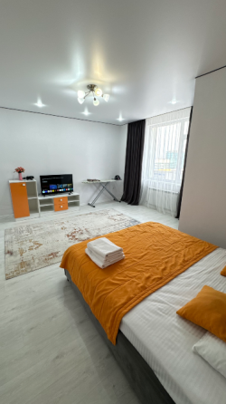 Комната с оранжевой кроватью и светлыми стенами, оформленная в современном стиле с большим окном