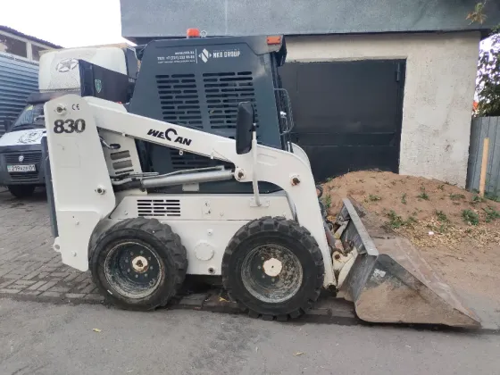 Мини-гусеничный погрузчик на улице рядом с бортом и кучей песка