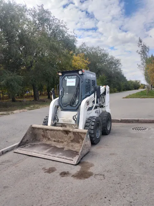 Мини-гусеничный погрузчик на дороге среди деревьев и под облачным небом