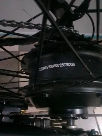 Үлкен дөңгелекті электрлік велосипед, рамада орнатылған аккумулятормен. Терезелері мен үстелі бар бөлмеде орналасқан.