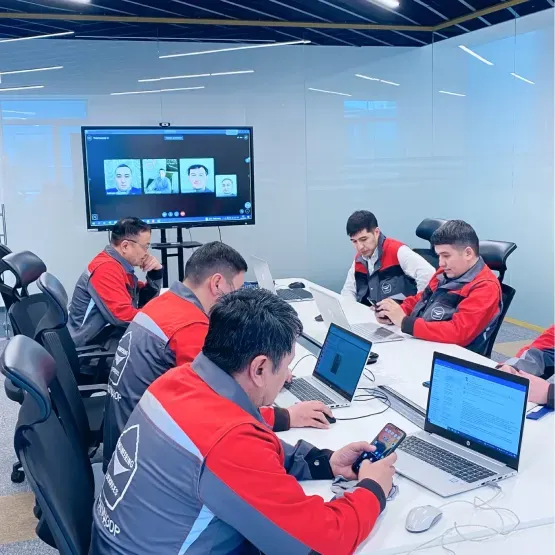 Команда сотрудников на собрании за столом с компьютерами и экраном для видеосвязи