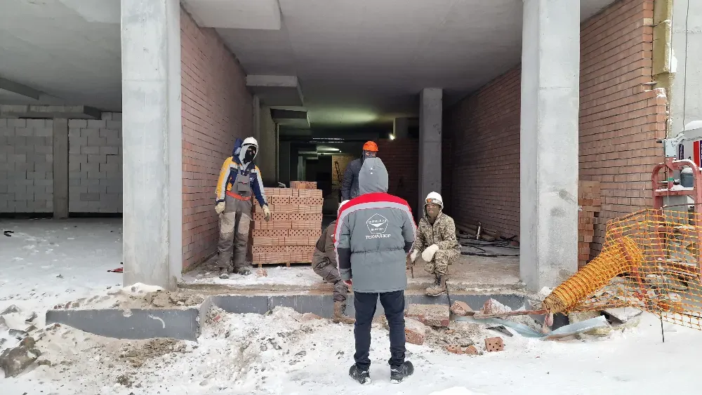 Құрылыс нысанында қыста кірпіштермен жұмыс істеп жатқан жұмысшылар