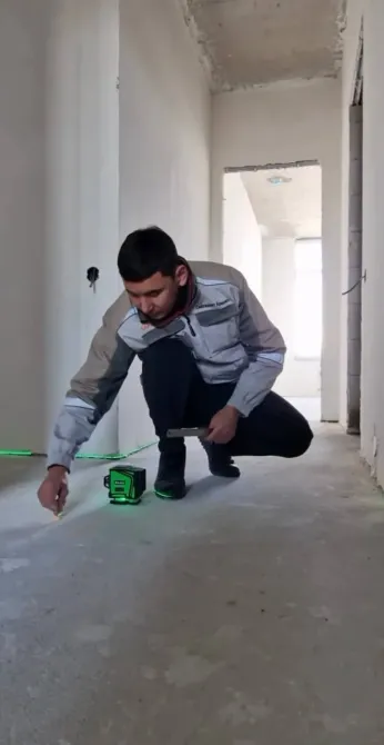 Рабочий делает измерения с лазерным уровнем на полу
