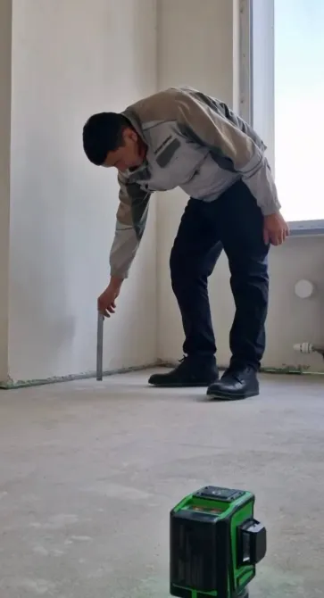 Рабочий устанавливает лазерный уровень на пол