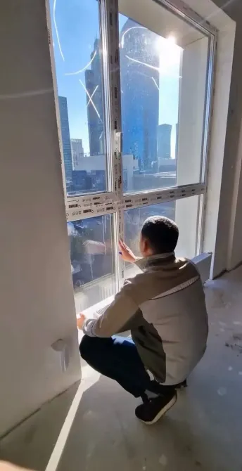 Рабочий устанавливает окно с видом на городской пейзаж