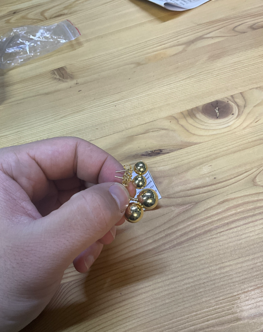 Человек показывает серьги с несколькими шарами и ценники на деревянном столе