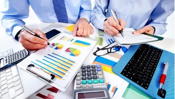 Работа сотрудников с отчетами и графиками на столе, калькулятор и ноутбук рядом, деловая обстановка