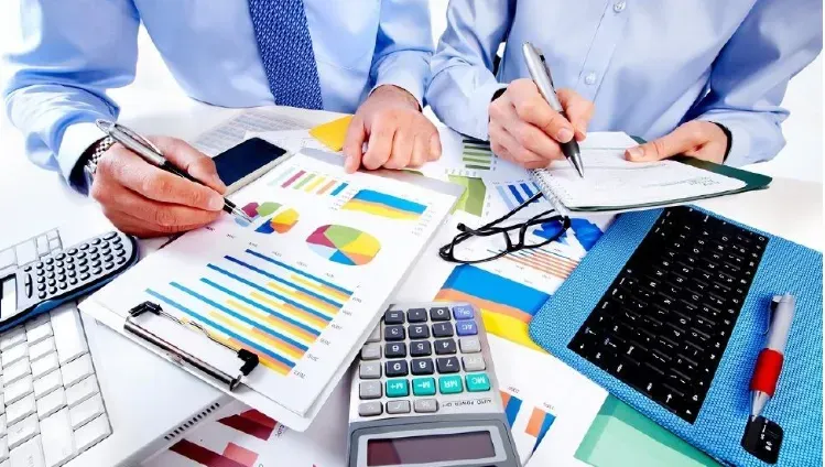 Работа сотрудников с отчетами и графиками на столе, калькулятор и ноутбук рядом, деловая обстановка