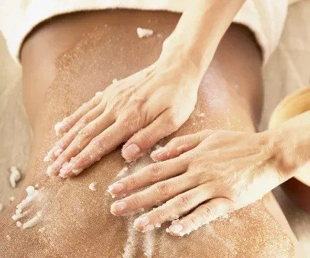 Массажистка наношает скраб на спину клиента с натуральными компонентами