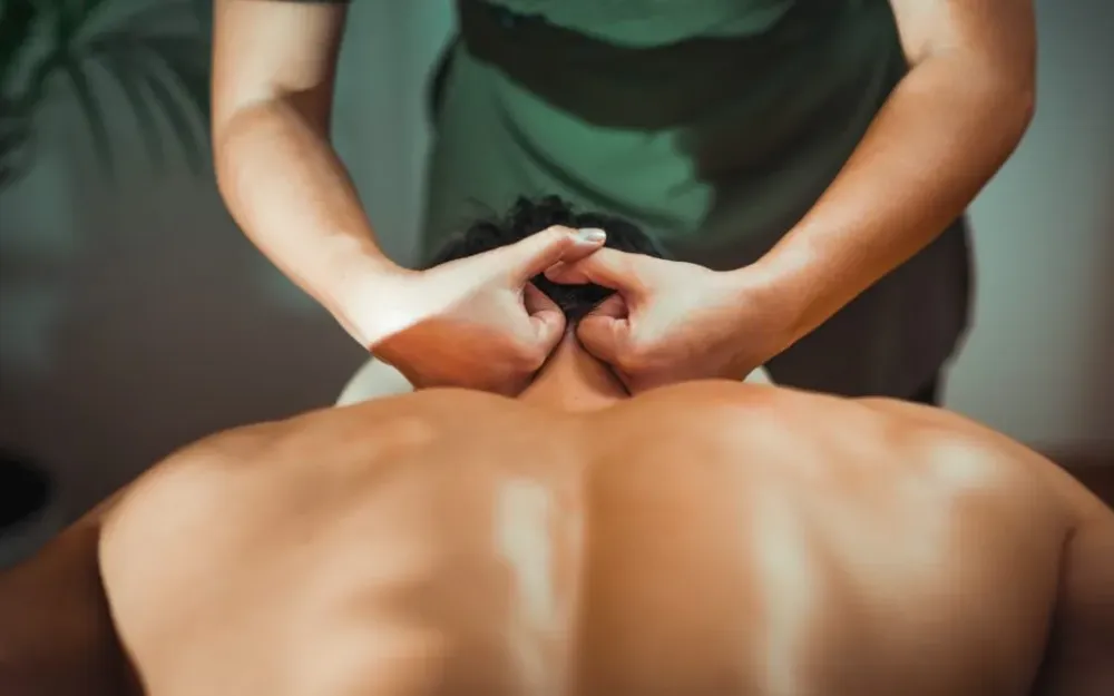 Массажист делает расслабляющий массаж шеи человеку, находящемуся на массажном столе